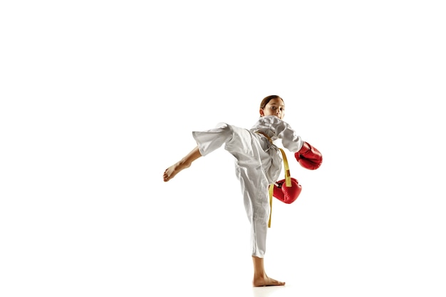 Confident junior in kimono practicing hand-to-hand combat, martial arts. Young female fighter with yellow belt s training on white wall. Concept of healthy lifestyle, sport, action.