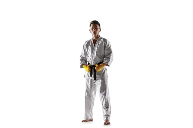 Confident korean man in kimono practicing hand-to-hand combat, martial arts. Young male fighter with black belt training isolated on white studio background. Concept of healthy lifestyle, sport.