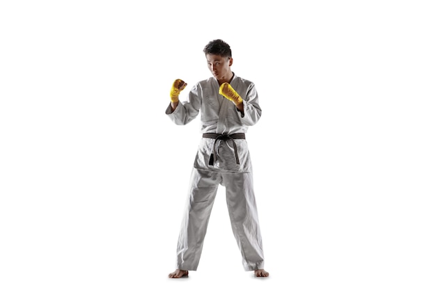 Confident korean man in kimono practicing hand-to-hand combat, martial arts. Young male fighter with black belt training isolated on white wall. Concept of healthy lifestyle, sport.