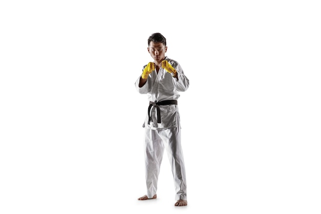 Уверенный в себе кореец в кимоно, практикующий рукопашный бой, боевые искусства. Молодой мужчина-боец с тренировкой черного пояса, изолированной на белой стене. Концепция здорового образа жизни, спорта.