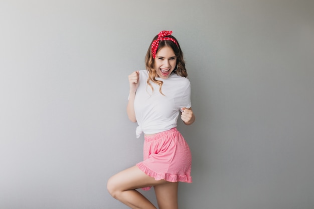 Confident lady in summer attire expressing positive emotions. Pretty female model in pink shorts dancing.