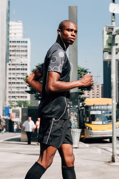 A confident male athlete fit young man jogging on road listening the music on earphone