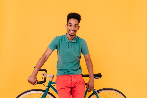 노란색 인테리어와 함께 포즈 자신감 남성 사이클. 자전거와 수염 된 아프리카 남자의 실내 샷.