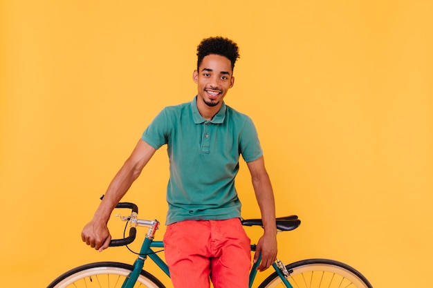 Confident male cyclist posing with yellow interior. Indoor shot of bearded african man with bicycle.