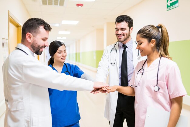 Confident male and female doctors stacking hands while standing in corridor at hospital