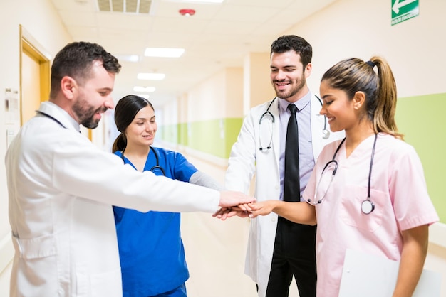 Confident male and female doctors stacking hands while standing in corridor at hospital