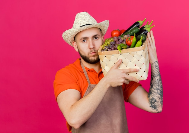 Free photo confident male gardener wearing gardening hat holds vegetable basket on shoulder