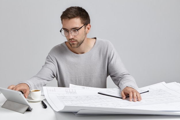 Free photo confident male worker looks attentively into tablet computer, work at construction project