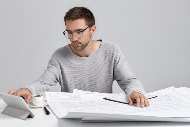 Уверенный мужчина-рабочий внимательно смотрит в планшетный компьютер, работает на строительном объекте
