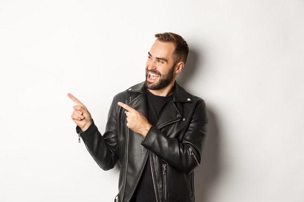 Confident  man in black leather jacket, pointing fingers left at promo offer, showing logo