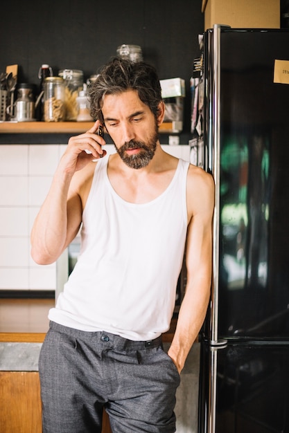 Confident man talking smartphone in kitchen