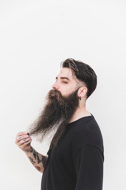 Confident man touching his beard standing against white backdrop