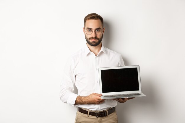 Confident manager demonstrating presentation on screen, showing laptop display and looking serious, standing  