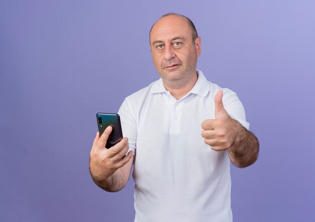 confident mature businessman looking at front holding mobile phone and showing thumb up