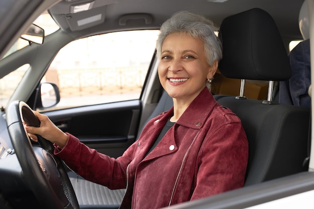 Confident mature businesswoman in stylish jacket driving car on city streets