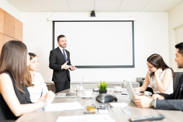 Уверенный в себе взрослый бизнесмен делает презентацию коллегам в зале заседаний