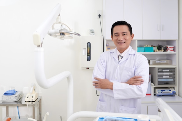 Уверенно среднего возраста азиатских мужчин стоматолог позирует в клинике