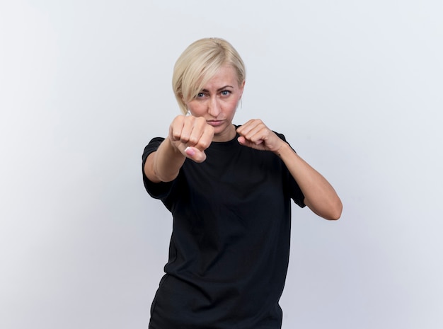 Confident middle-aged blonde slavic woman looking at camera doing boxing gesture isolated on white background with copy space