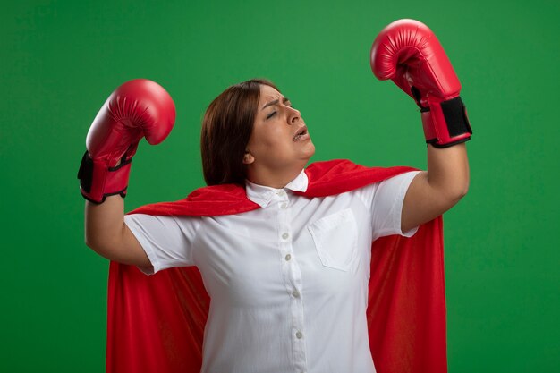 녹색 배경에 고립 된 포즈 싸움에 서 권투 장갑을 끼고 자신감 중년 슈퍼 히어로 여성