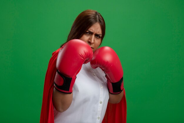 Уверенная женщина-супергерой средних лет в боксерских перчатках, стоящая в боевой позе, изолированной на зеленом