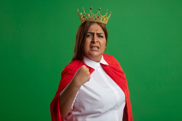 Confident middle-aged superhero female wearing crown showing yes gesture isolated on green background