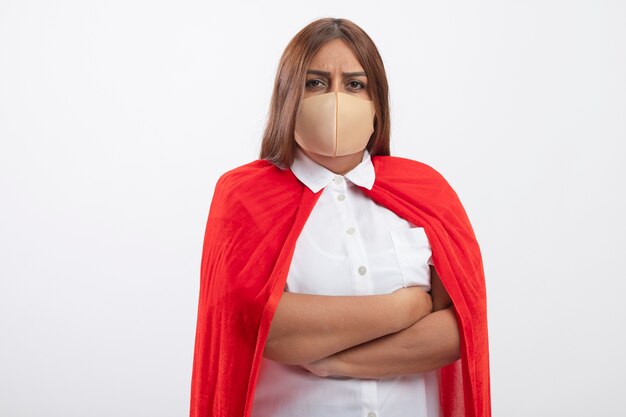 Confident middle-aged superhero female wearing medical mask crossing hands isolated on white