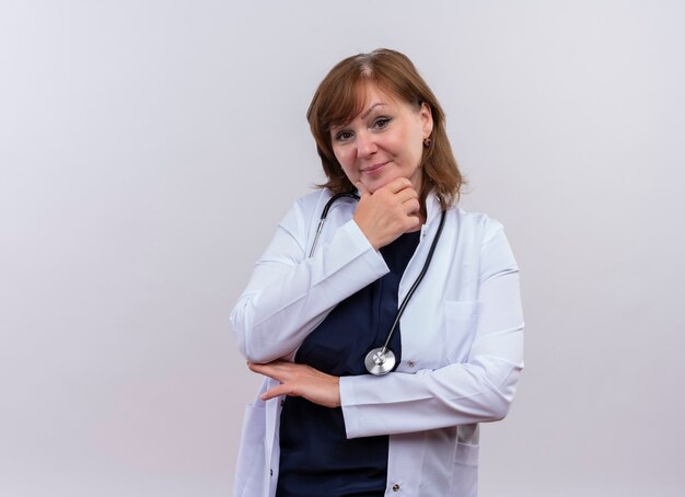 自信を持って中年女性医師が医療用ローブとコピースペースで孤立した白い壁のあごに手を置く聴診器を着て