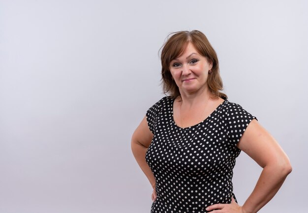 Confident middle-aged woman putting hands on waist on isolated white wall with copy space