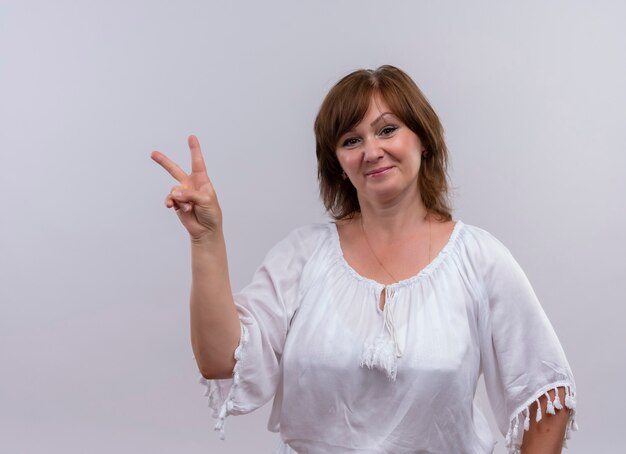 Confident middle-aged woman showing peace sign on isolated white wall