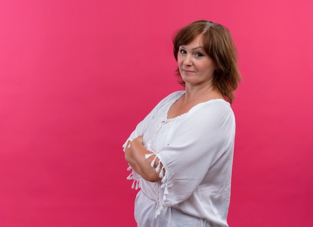 Confident middle-aged woman standing with closed posture on isolated pink wall