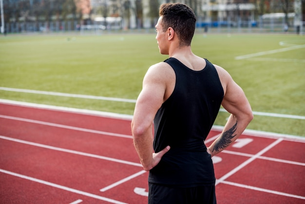 Confident muscular male athlete on red race track looking away