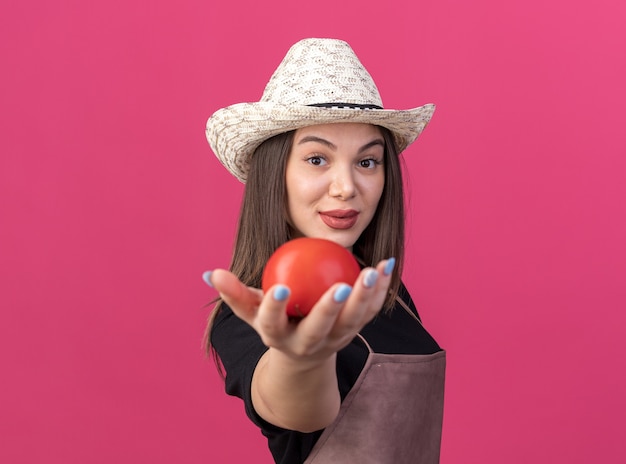 ピンクのトマトを差し出してガーデニング帽子をかぶって自信を持ってかなり白人女性の庭師