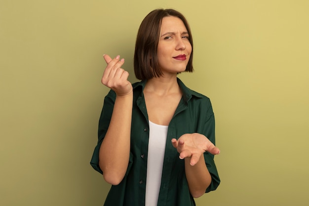 La donna abbastanza caucasica sicura tiene la mano aperta e gesti il segno della mano dei soldi su verde oliva