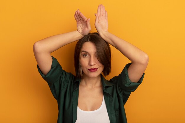 Confident pretty caucasian woman holds hands over head gesturing hare ears on orange