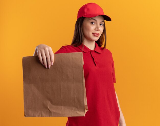Confident pretty delivery woman in uniform holds paper package