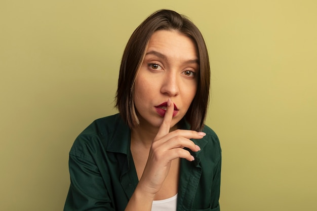 Confident pretty woman doing silence gesture isolated on olive green wall