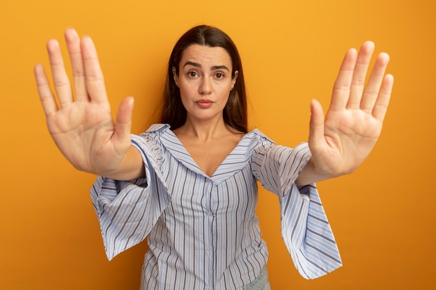 Foto gratuita gesti di donna graziosa sicura fermare il segno della mano con due mani isolate sulla parete arancione