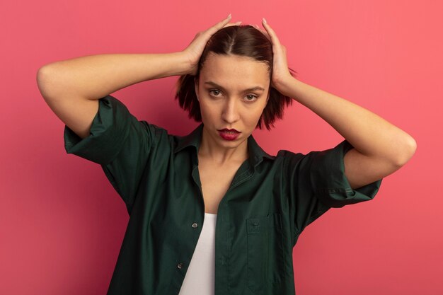 Confident pretty woman holds head and looks at front isolated on pink wall