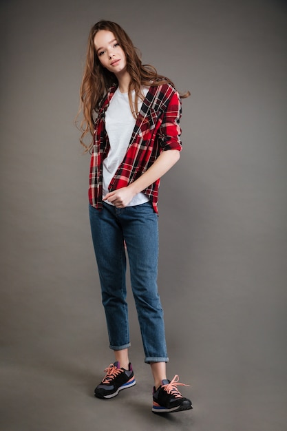 Confident pretty young woman in plaid shirt and jeans standing