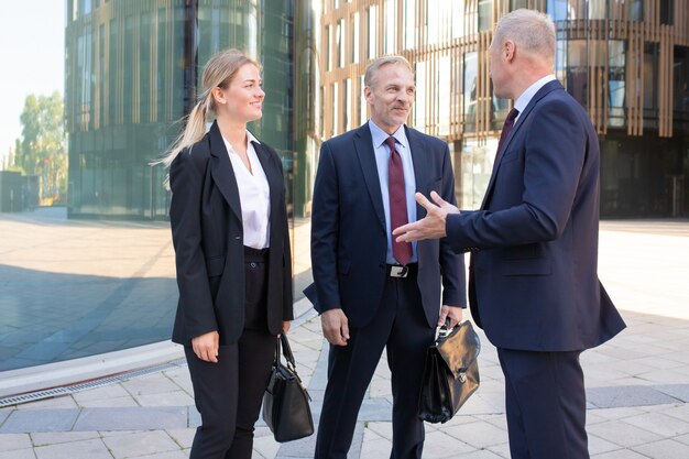 Confident professional adult businesspeople meeting outdoors. Content business man and woman in suit listening boss and smiling. Teamwork, negotiation and partnership concept