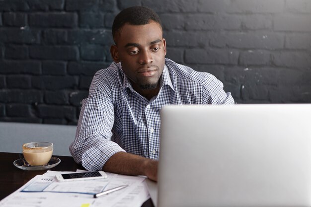 Confident prosperous African-American young top-manager wearing formal shirt having coffee