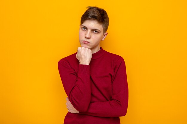 Confident putting fist under chin young handsome guy wearing red sweater 