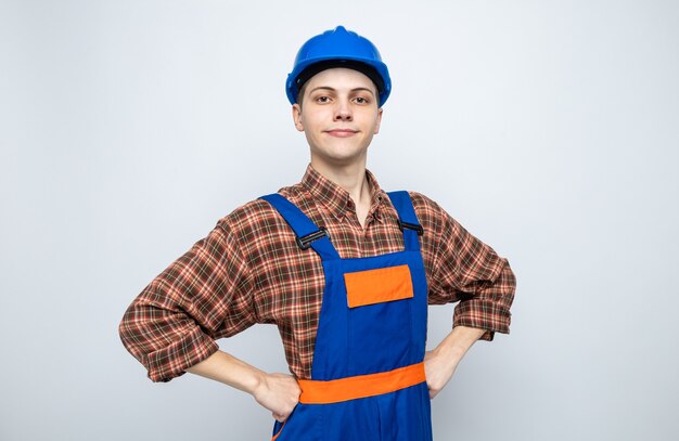 Free photo confident putting hands on hip young male builder wearing uniform