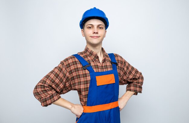 Foto gratuita fiducioso di mettere le mani sull'anca giovane costruttore maschio che indossa l'uniforme