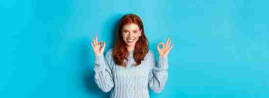 Free photo confident redhead girl showing okay signs praising choice approve and agree like something standing