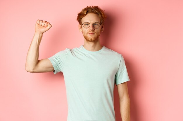 Confident redhead man standing united with black lives matter movemet, showing raised fist and looking serious at camera, protesting and being an activist, standing over pink background.