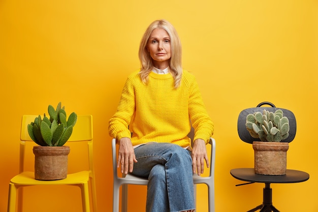 Free photo confident serious female pensioner poses between two chairs with cactus