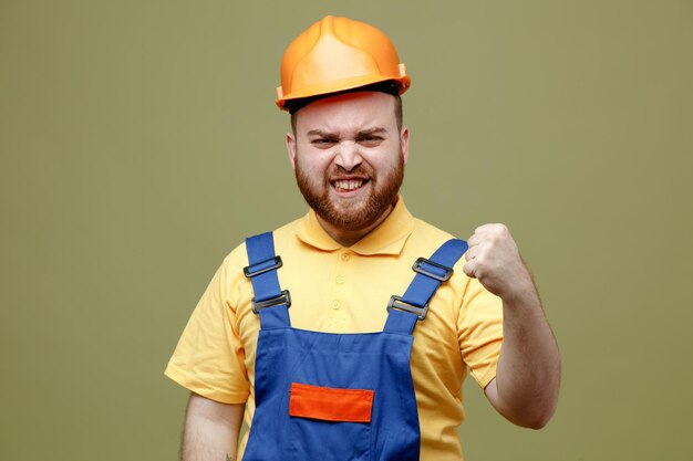 Confident showing strong gesture young builder man in uniform isolated on green background
