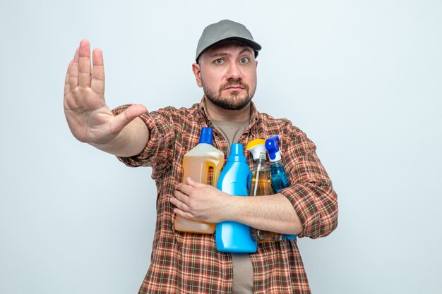 Уверенный славянский уборщик, держащий чистящие спреи и жидкости, жестикулирующий со знаком остановки
