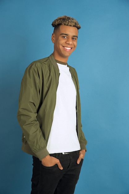 Confident and smiling. African-american man's portrait isolated on blue studio background. Beautiful male model in casual clothes. Concept of human emotions, facial expression, sales, ad. Copyspace.